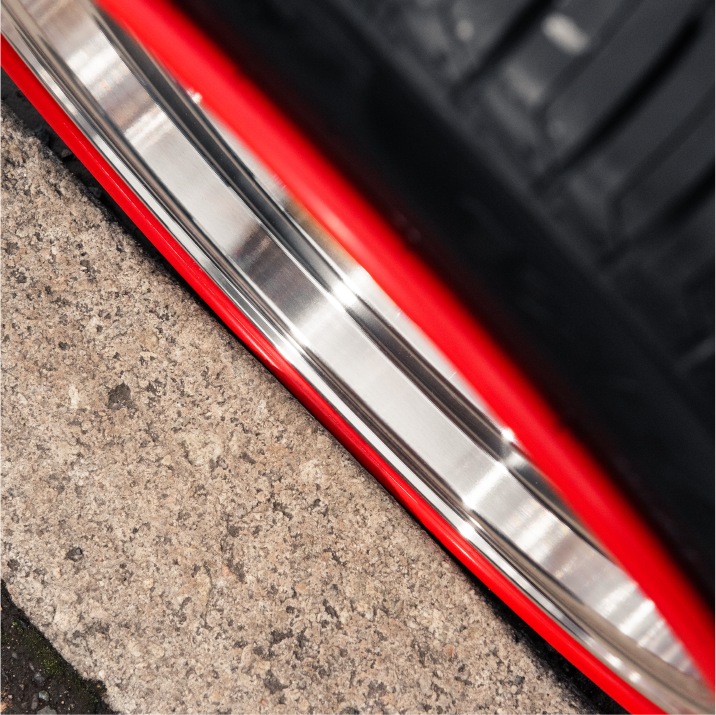 Image taken from above a wheel up against a curb, with sliver alloys and a red RIMFINITY continious wheel protecting band